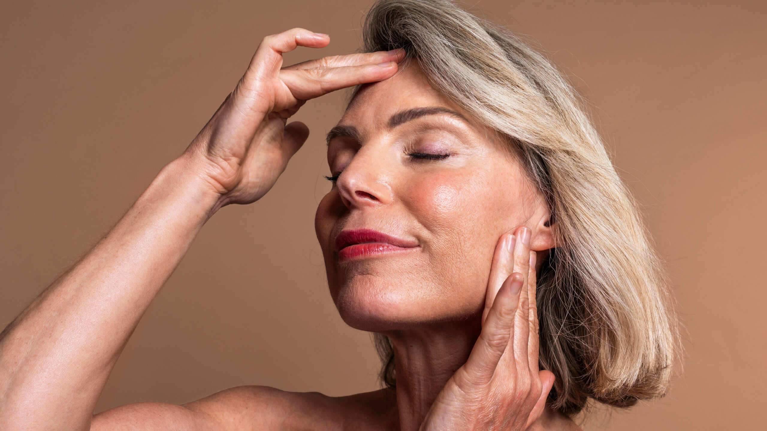 Beauty portrait of beautiful mature woman, concepts about cosmetics, skincare and wellness. Mature woman with closed eyes gently touching face, embodying graceful aging and radiant skin wellness