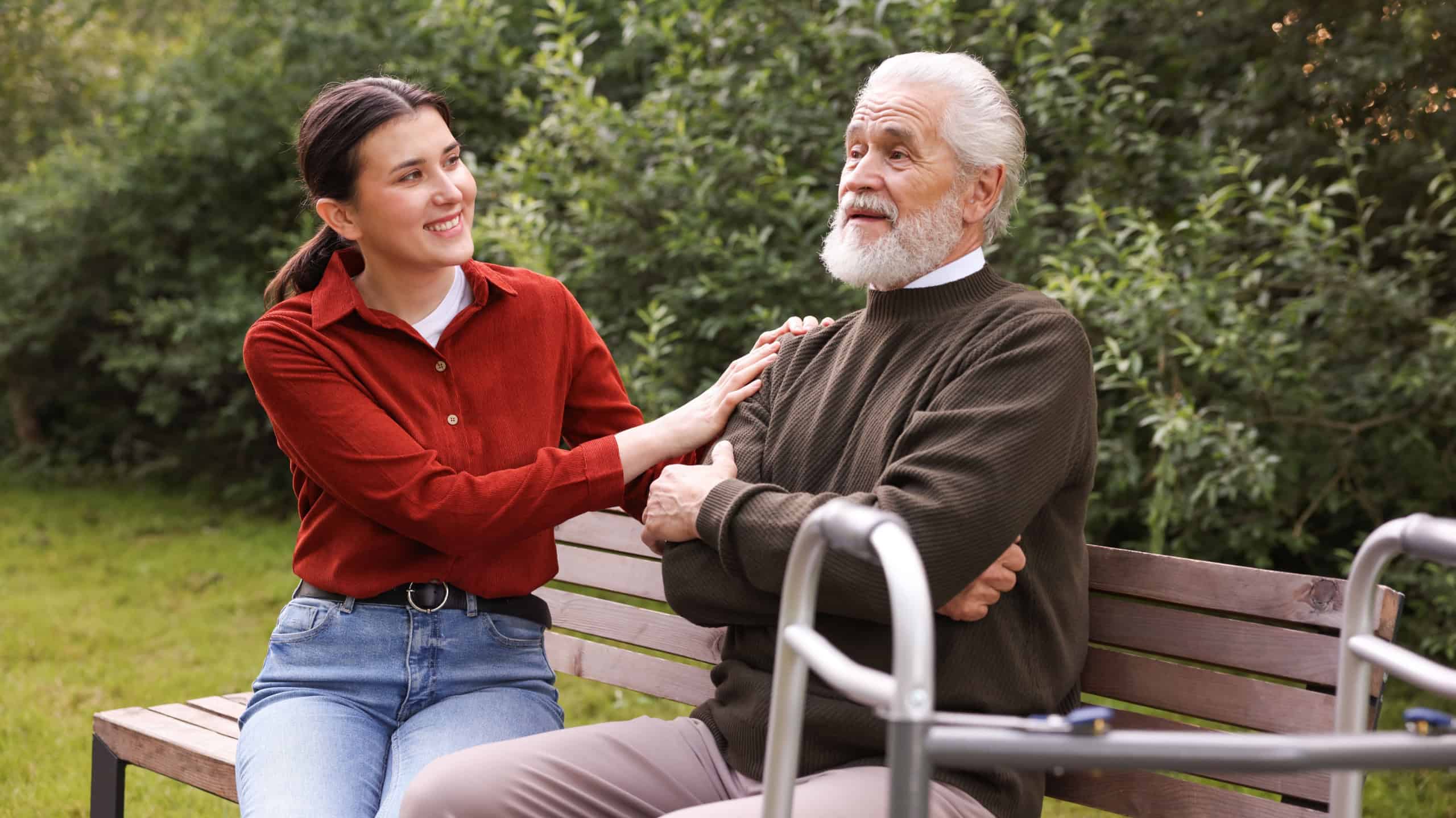 Smiling caregiver supporting elderly man with walking frame outdoors