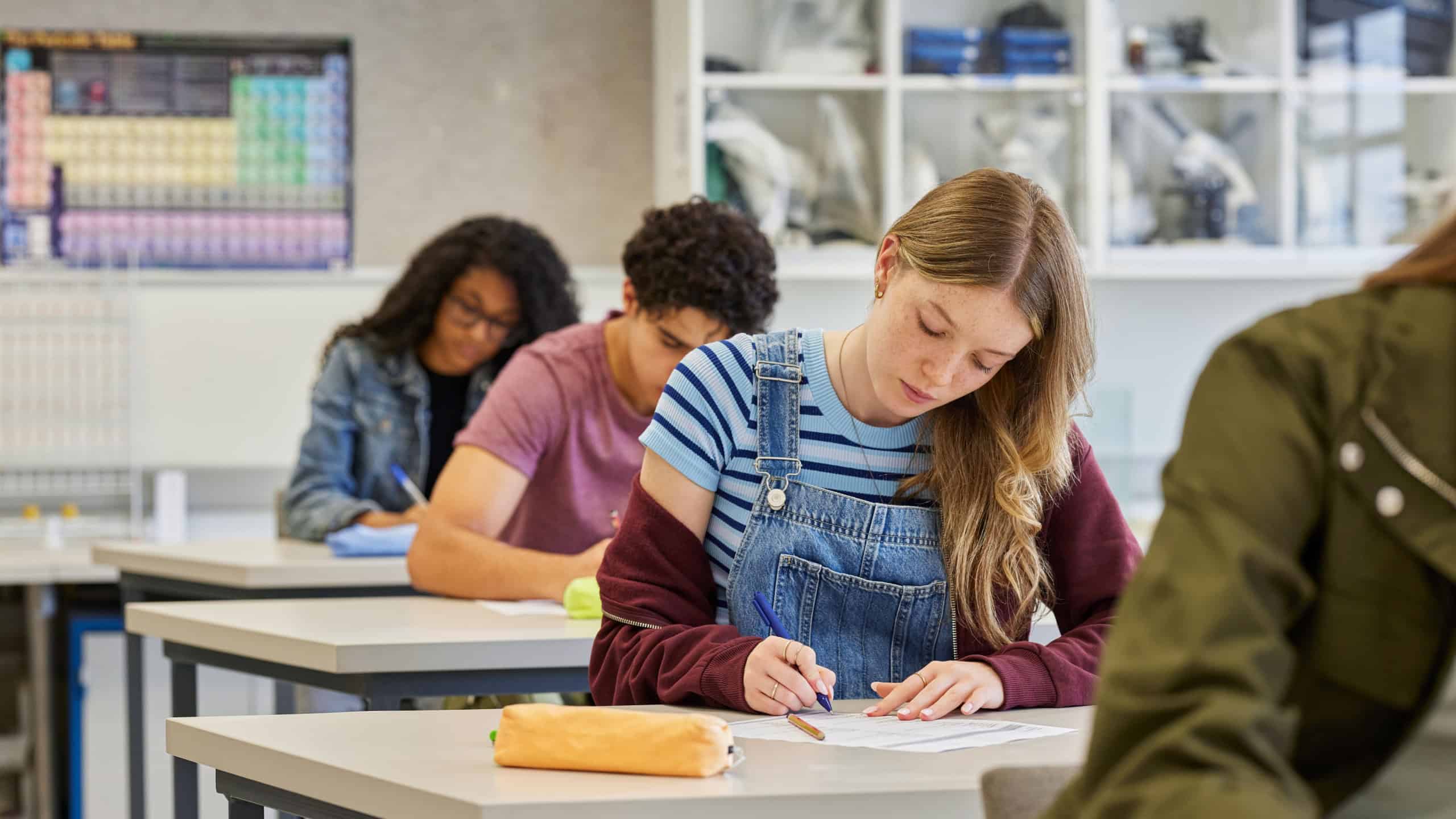 Focused female student complete a multiple choice quiz during classroom test sitting in a row. Serious casual girl concentrating on task in academic setting at high school.