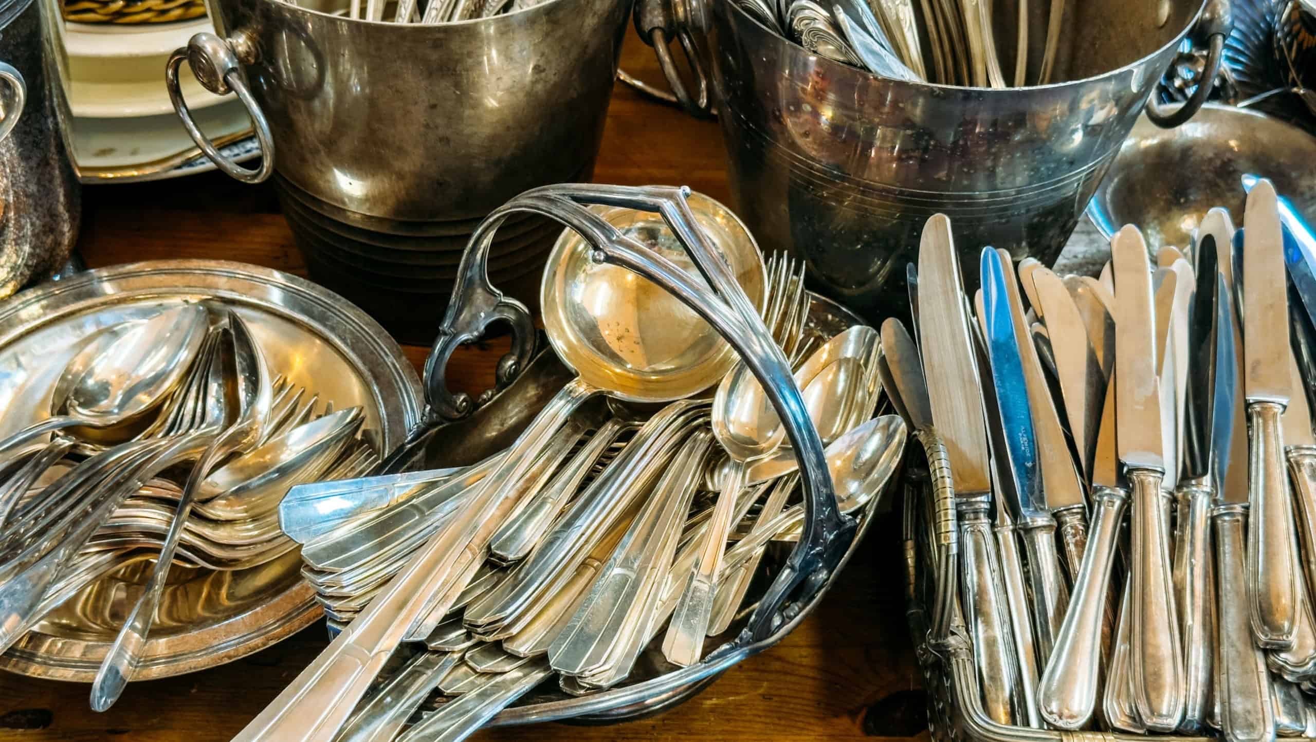 A collection of silver cutlery including knives, forks, and spoons arranged in baskets and trays. Secondhand cutlery, vintage flatware, elegant dining revival, heirloom tableware