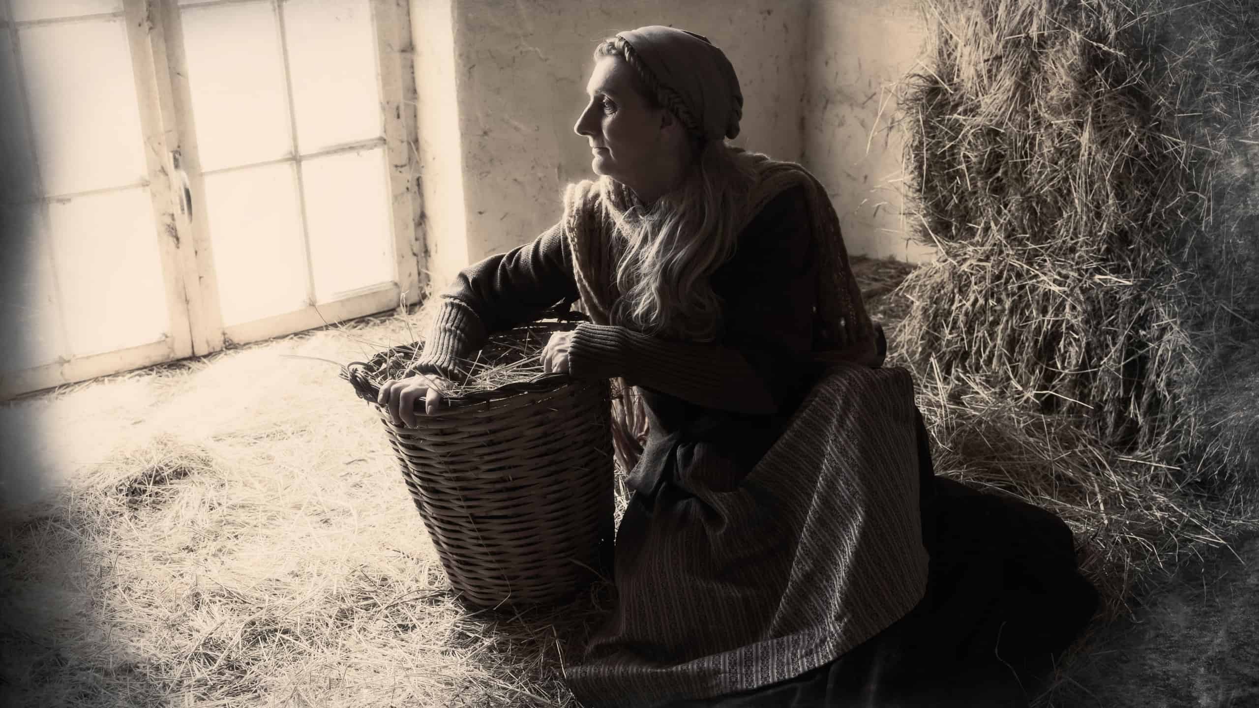 Woman in historical medieval costume posing with a wicker basket in a hay barn