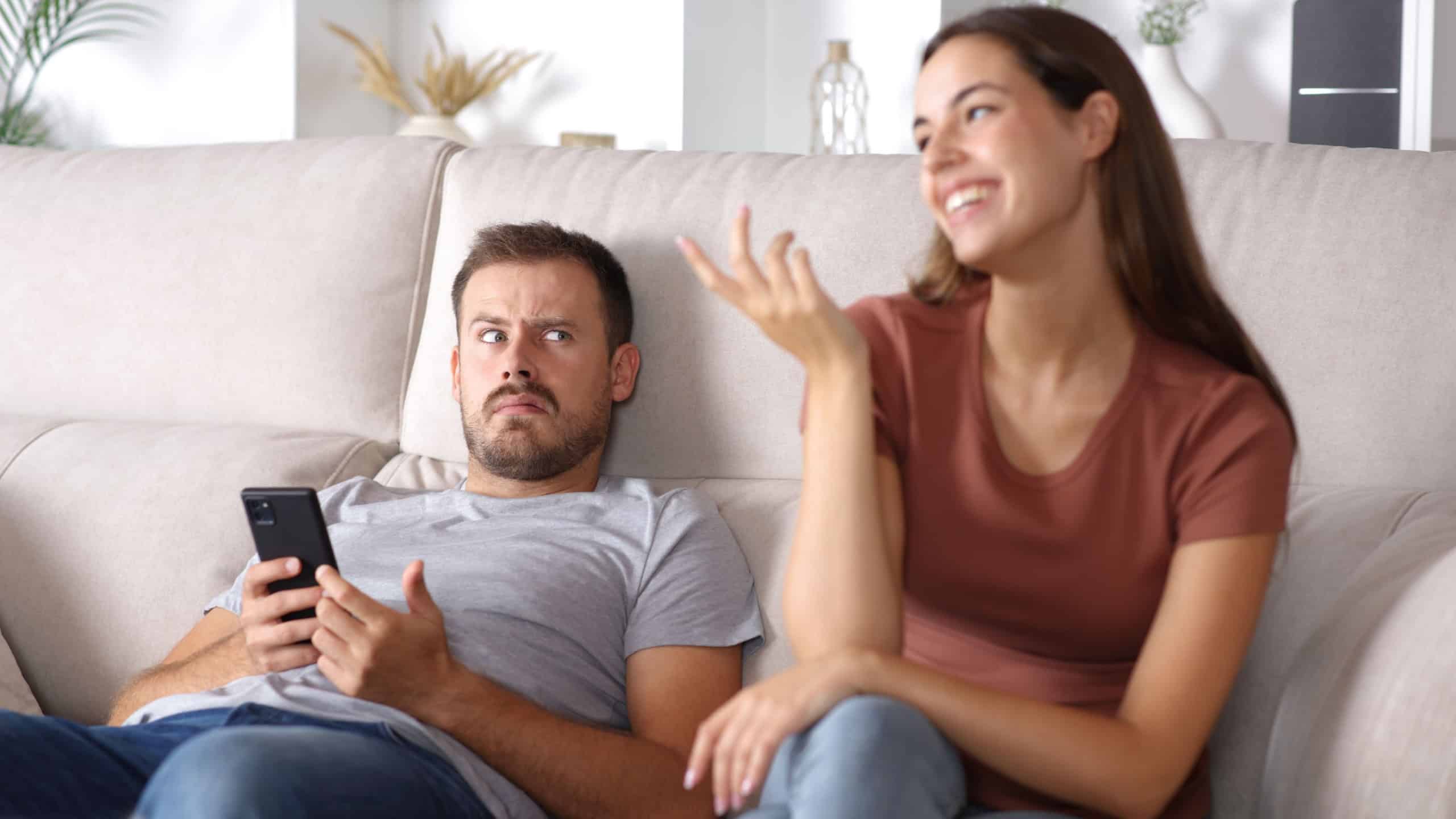 Shocked man listening to his partner sitting on a couch at home