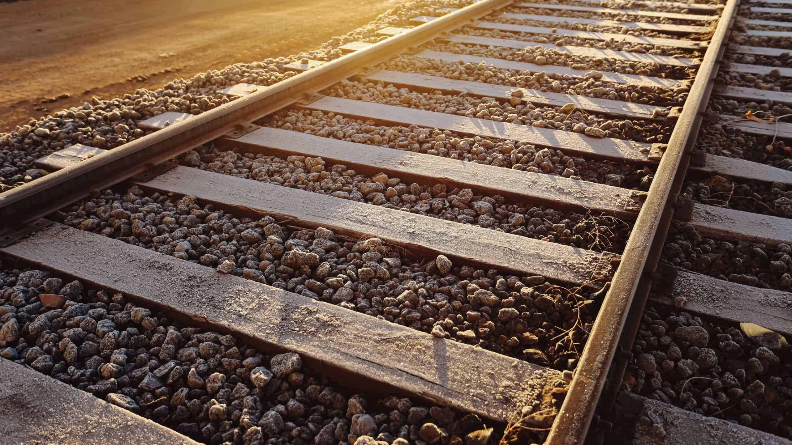 Railway tracks at sunset with warm golden light. Steel rails and wooden sleepers on gravel ballast. Perspective lines leading forward. Transportation infrastructure detail. Travel and journey concept