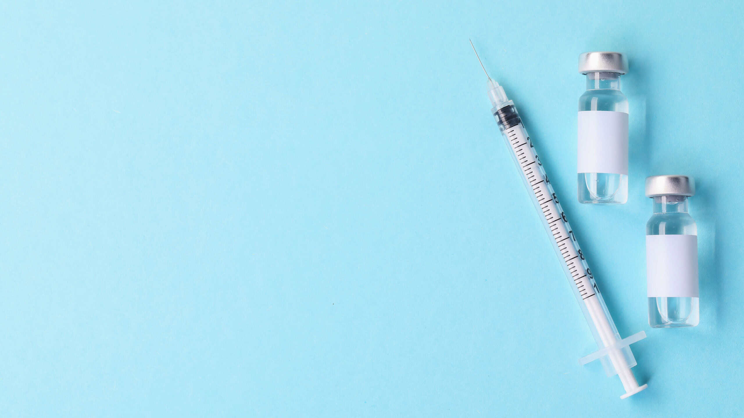 Vaccine in vials and syringe on light blue background, flat lay. Space for text