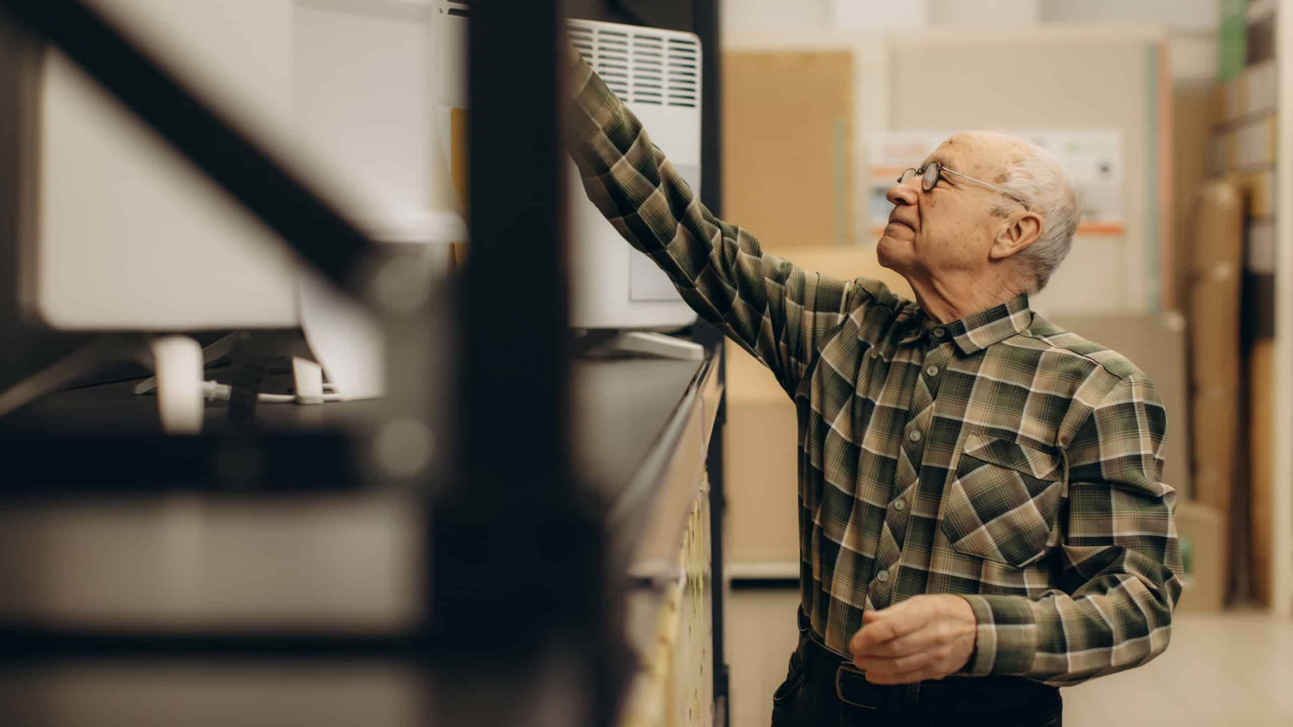 Elderly customer inspecting an electric heater on a shelf in a retail shop, making a purchase decision