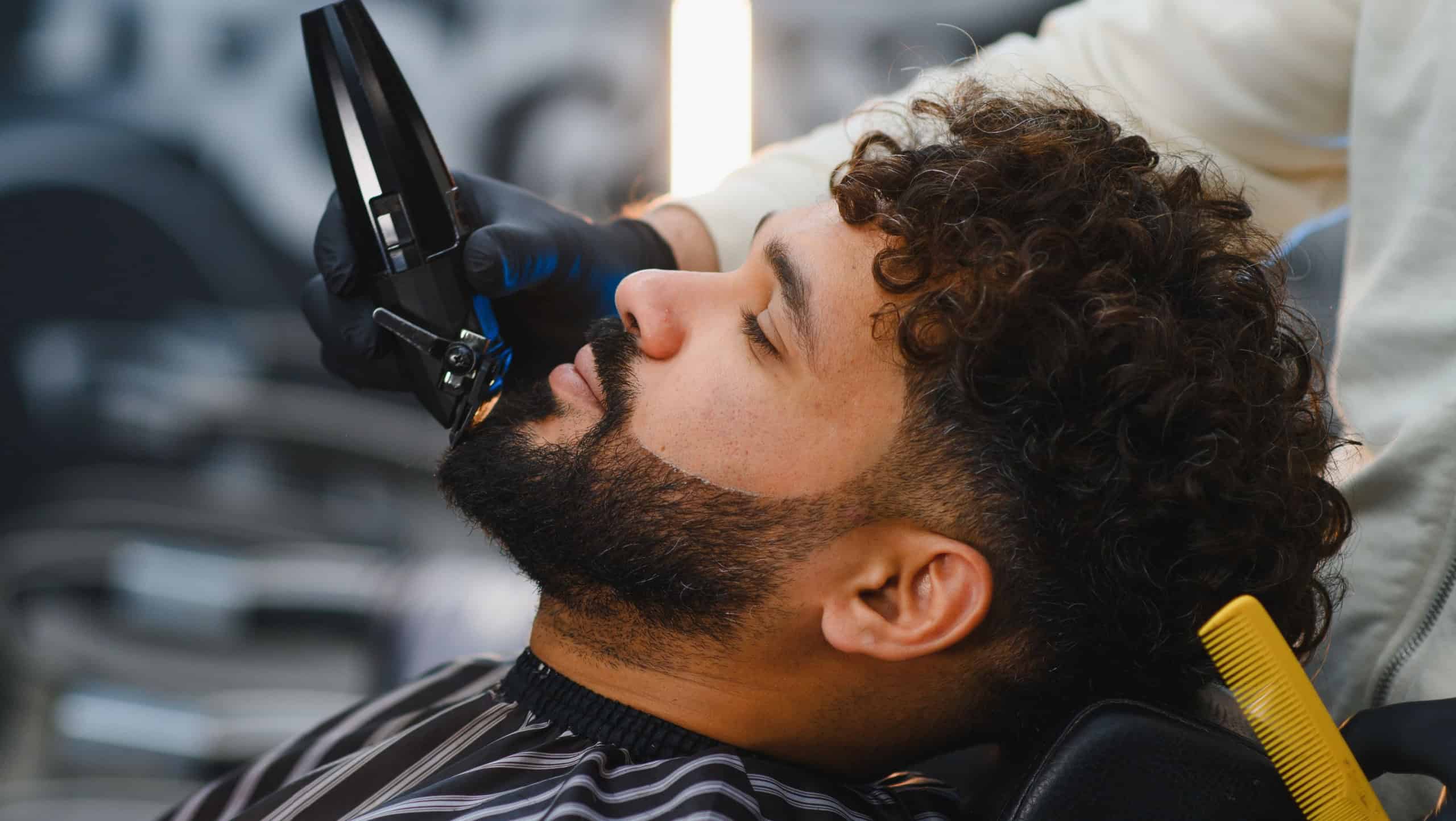 Man getting a precise fade haircut and beard trim from a barber with clippers in a modern, stylish barbershop salon