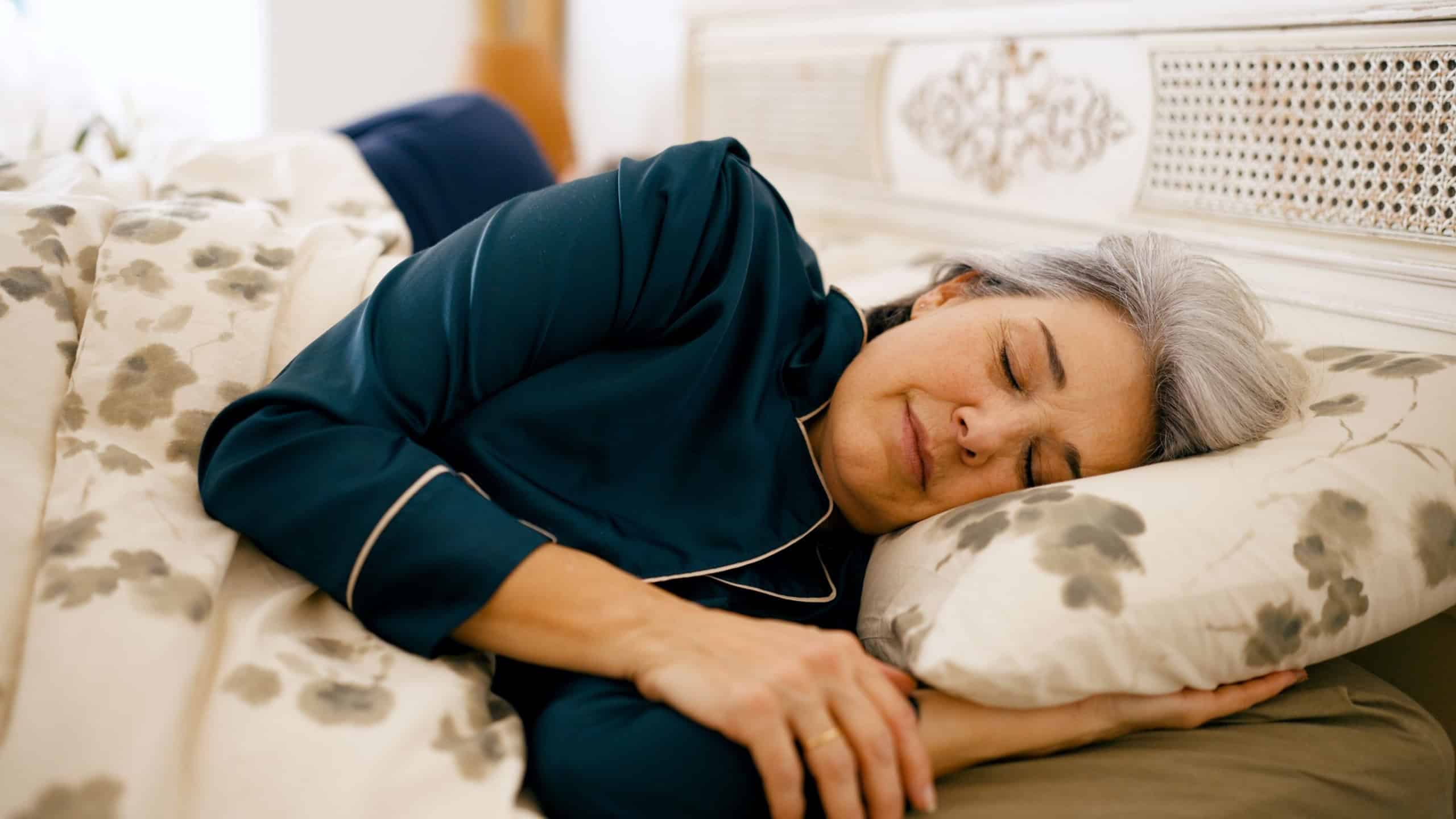 Senior woman resting comfortably in bed, wearing pajamas, enjoying a peaceful night's sleep in a cozy bedroom