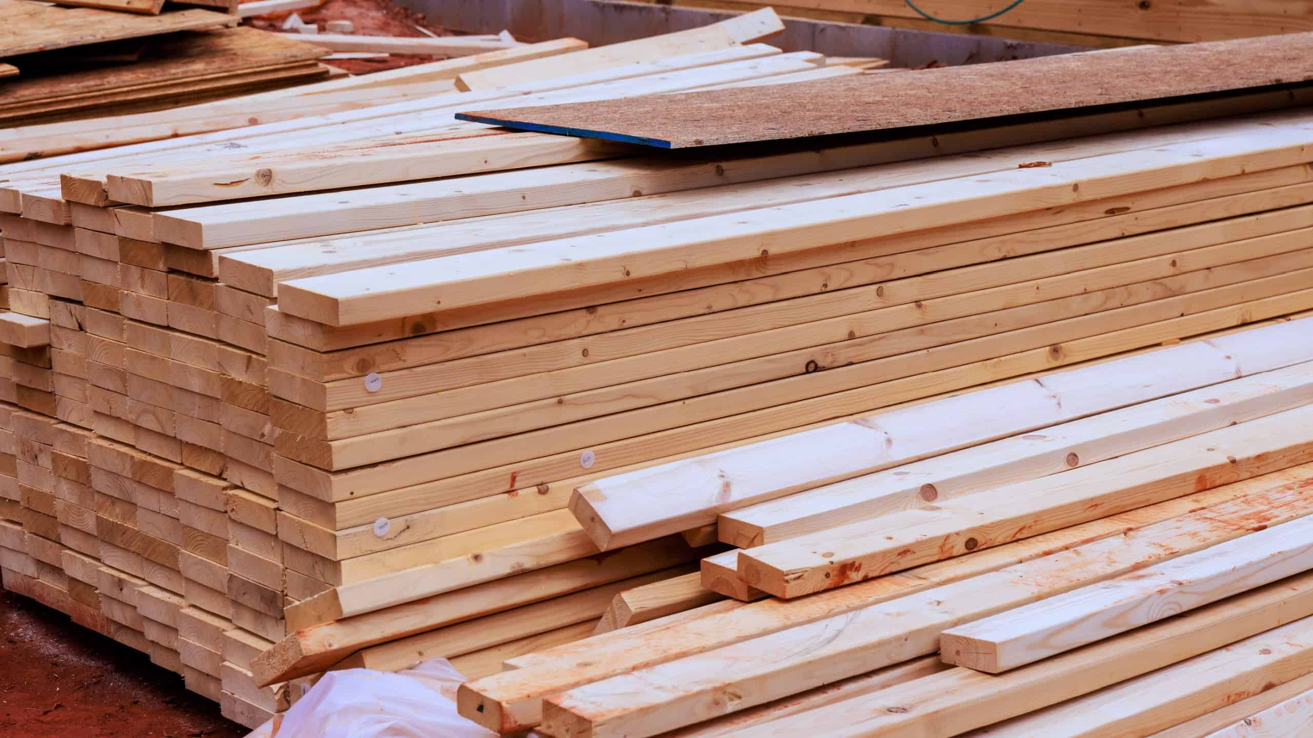 Wood planks are stacked on construction site with tools nearby as work continues on new home project