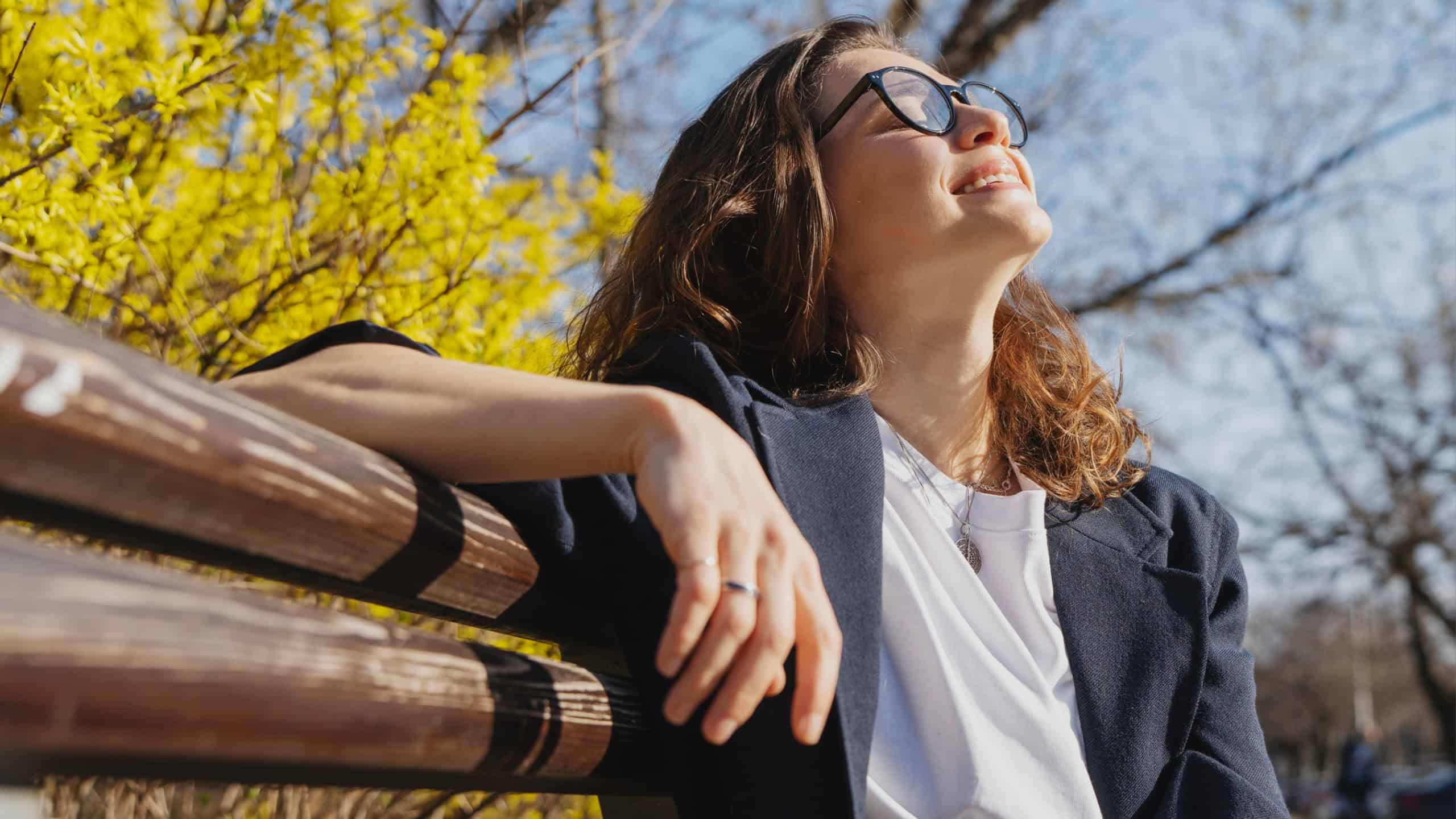 Relaxed young curly woman in glasses enjoying spring sun on a city bench