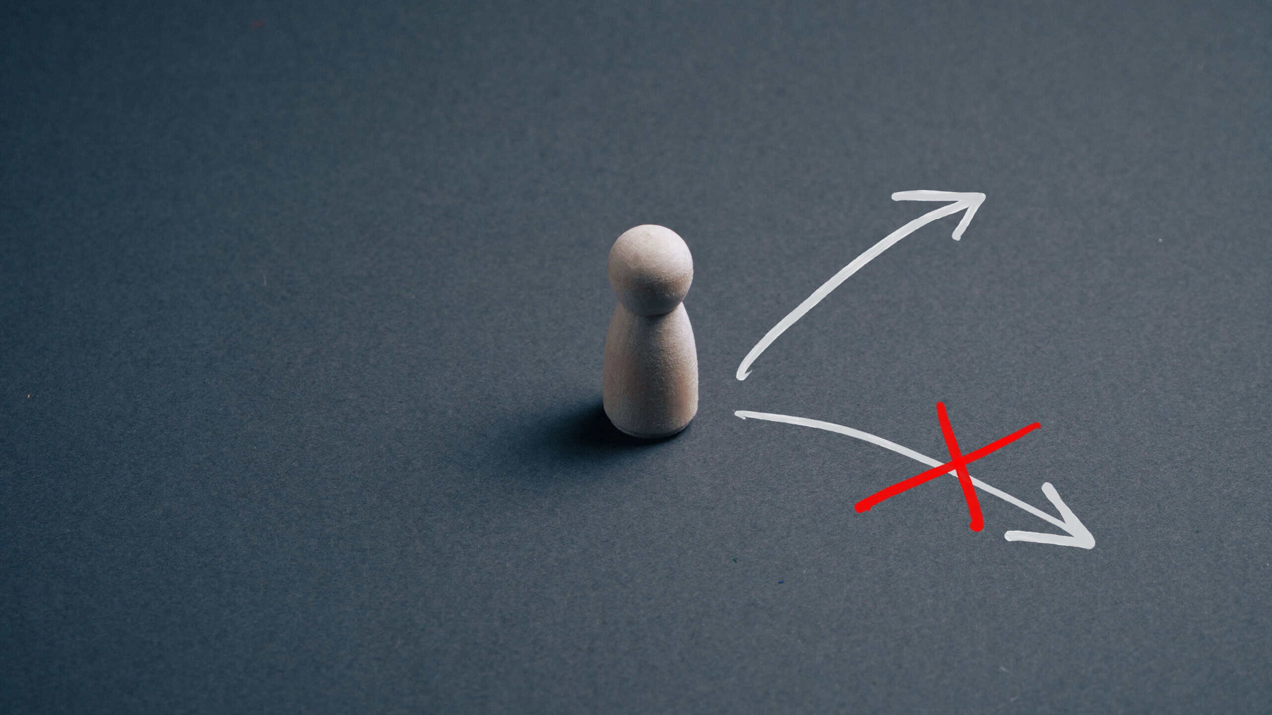 Wooden pawn beside diverging arrows with a red X marking the wrong direction — concept for business decision making, choosing the right path, leadership and career choices.