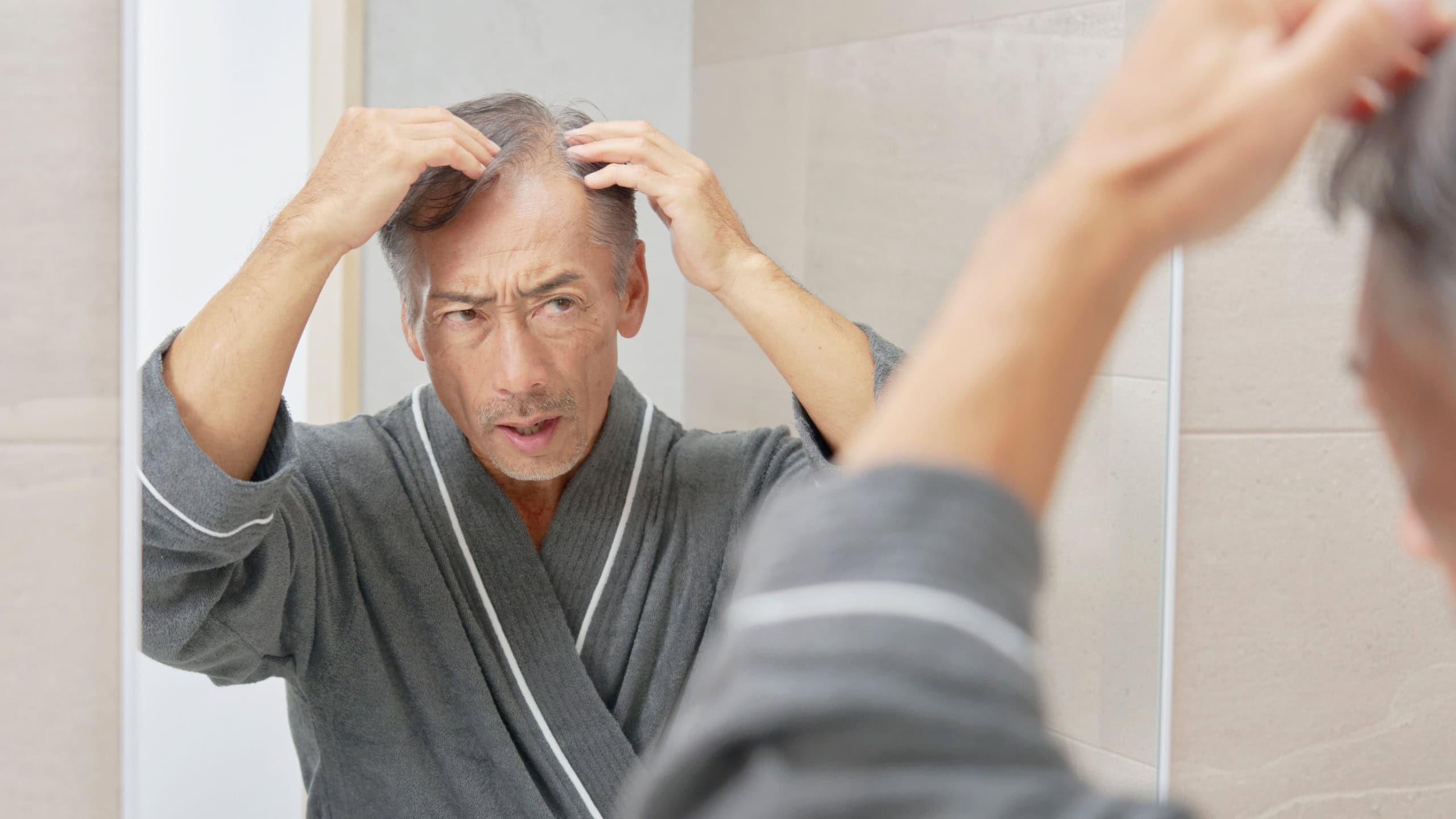 Asian senior man worrying about hair loss checking in mirror at bathroom