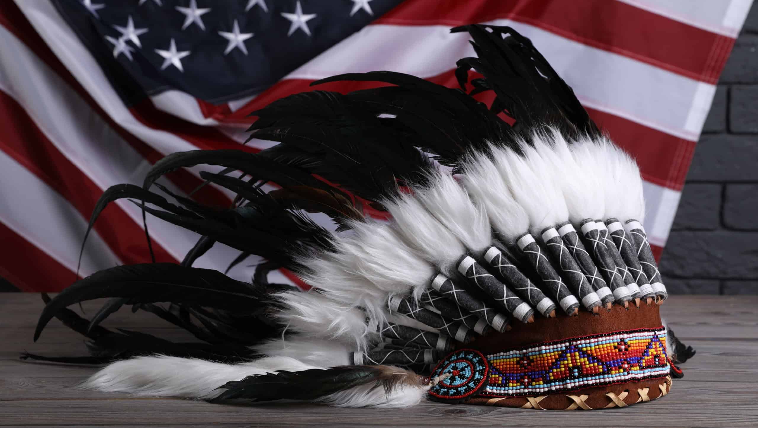 Native American chief headdress (feathered war bonnet) on wooden surface against American flag