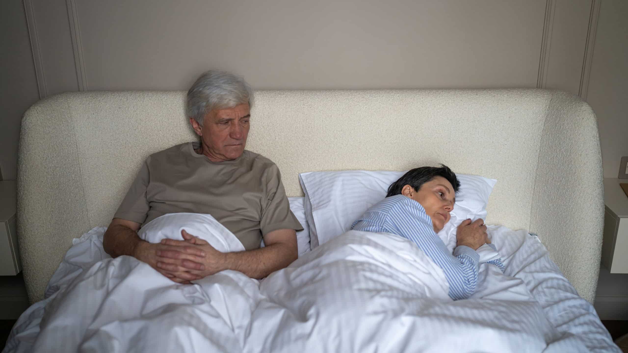 Senior married couple in conflict, elderly man and woman lying in bed with emotional tension after family brawl, wife using silent treatment manipulation and rejecting communications with husband.