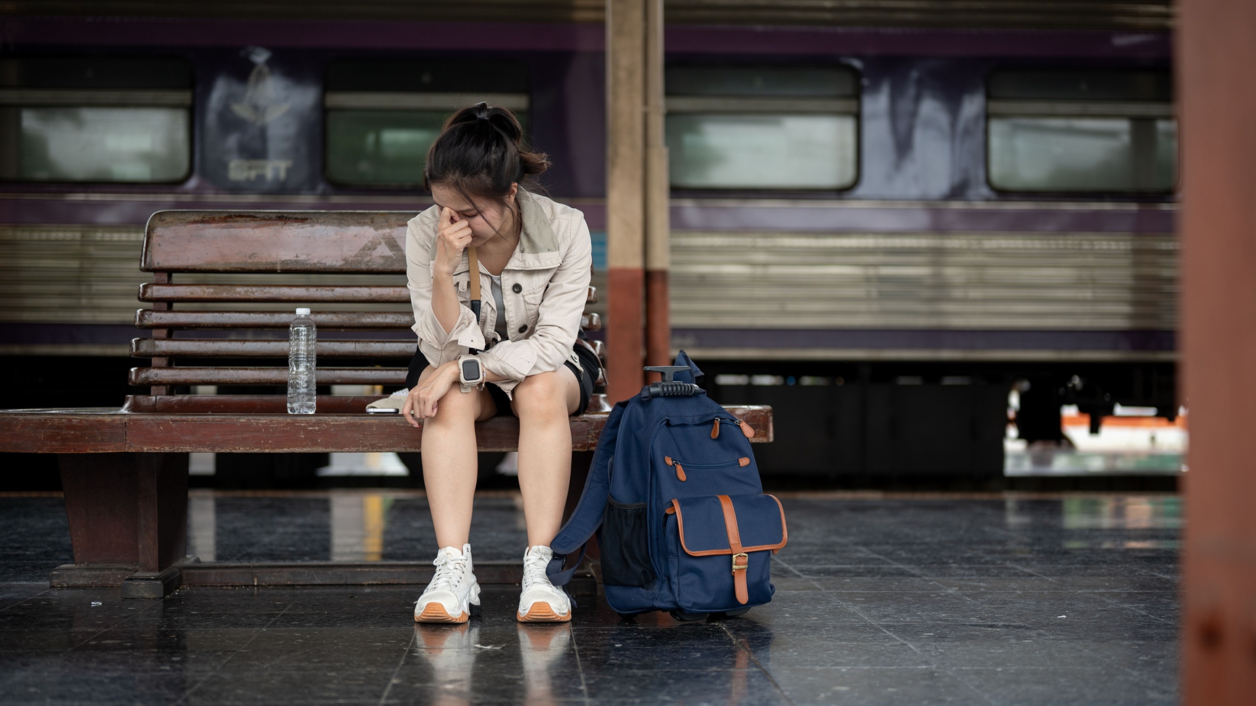 Asian female traveler sitting sadly on a station bench beside luggage while waiting for train. Solo Trip, Going Outdoor, Vintage transportation