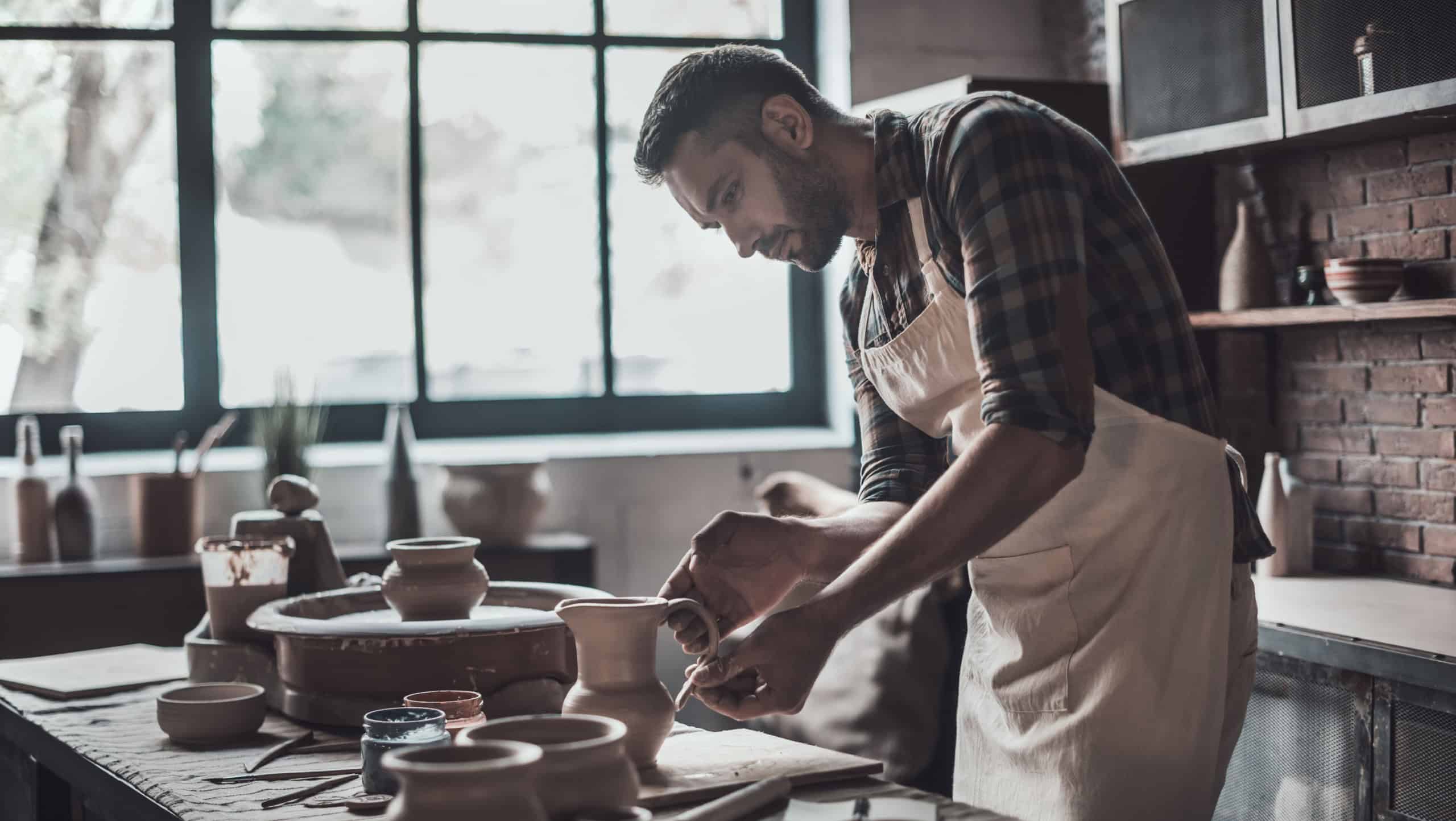 Potter making jug. Confident young man in apron making ceramic jug at his workshop