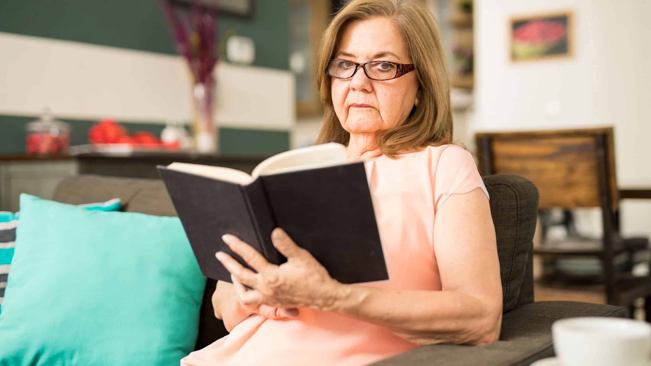 Elderly woman wearing glasses and relaxing at home while reading a book