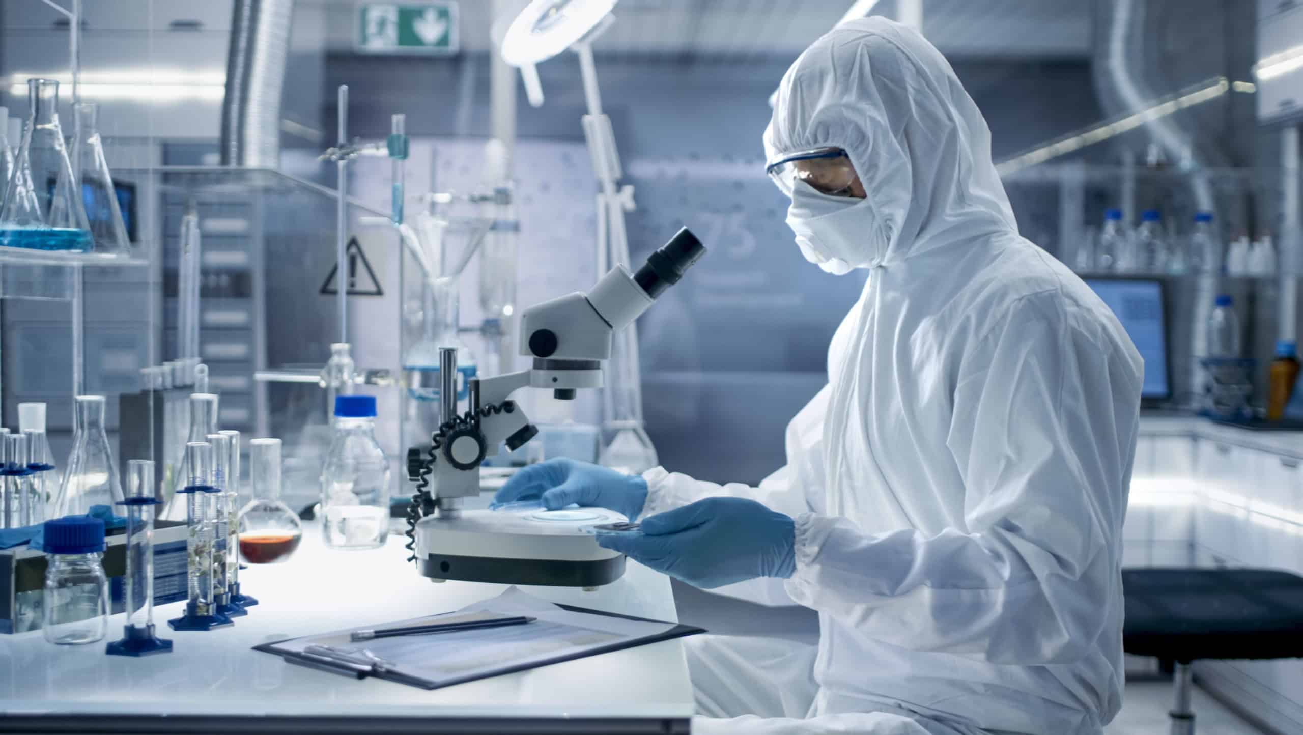 In a Secure High Level Laboratory Scientists in a Coverall Conducting a Research. Biologist Adjusts Samples in a Petri Dish with Pincers and Examines Them Under Microscope.