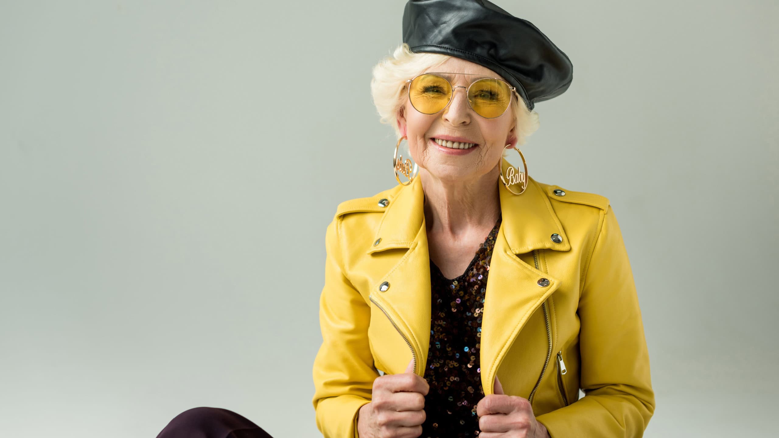 stylish senior woman in yellow jacket and leather beret, isolated on grey