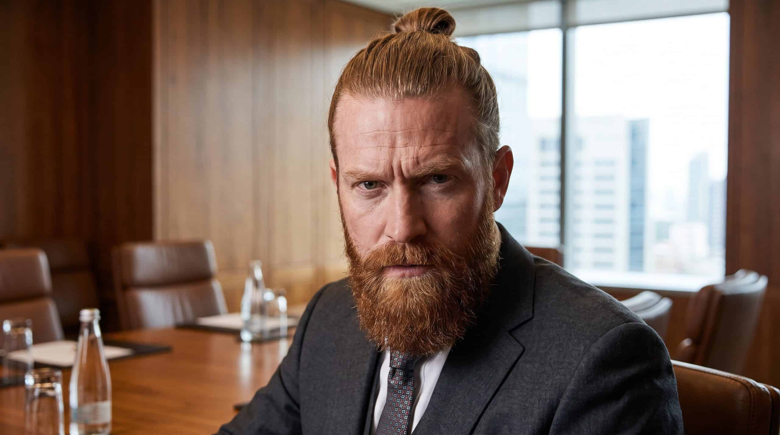 Portrait of attractive redhead Caucasian businessman with bun hairstyle and thick beard wearing formal suit looking at camera with confident serious expression before important meeting or negotiations