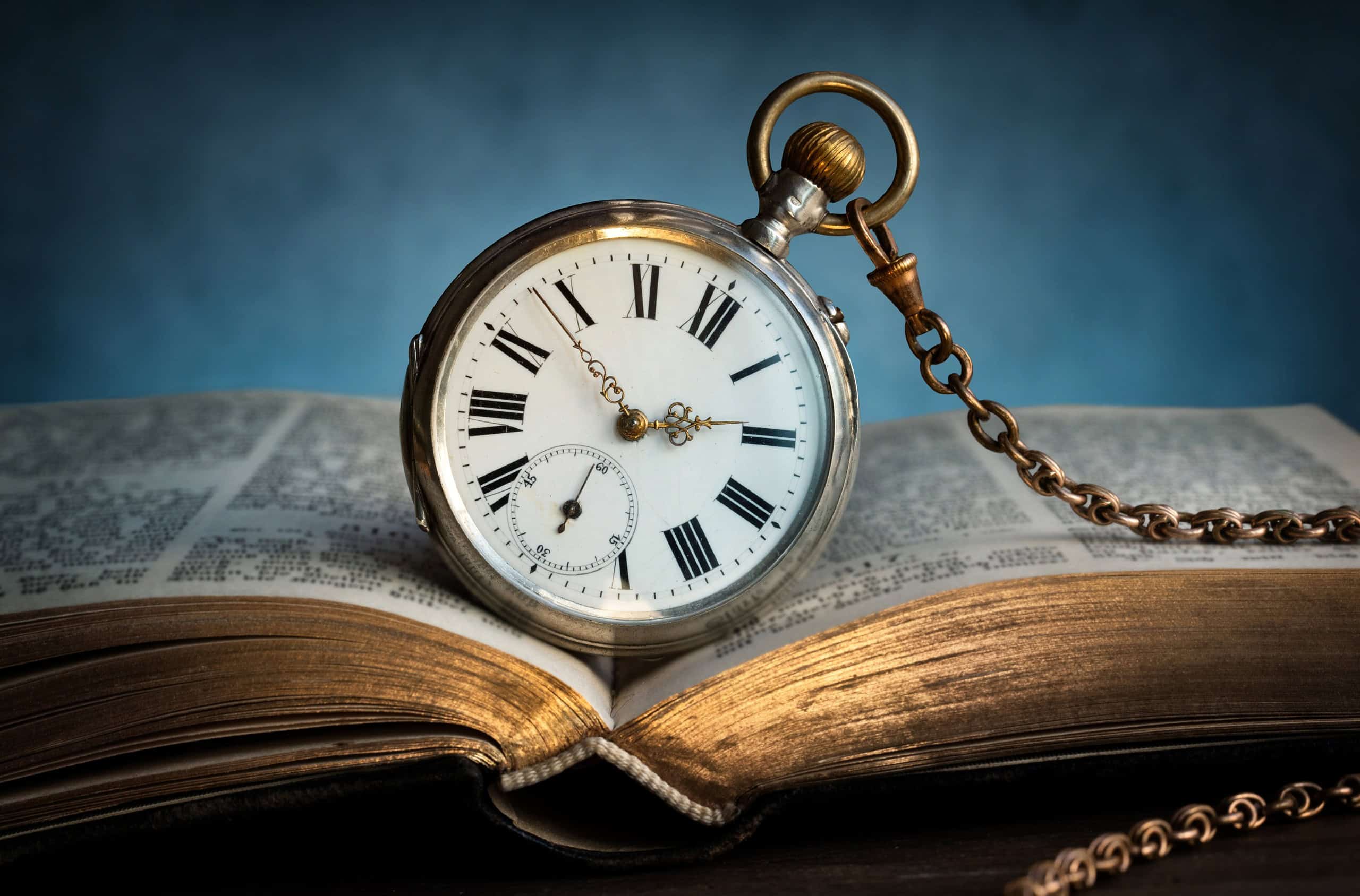 The clock lies on an old book. Clock as a symbol of time, the book is a symbol of knowledge and science. Concept of time, history, science, memory, information. Vintage watch, clock background.