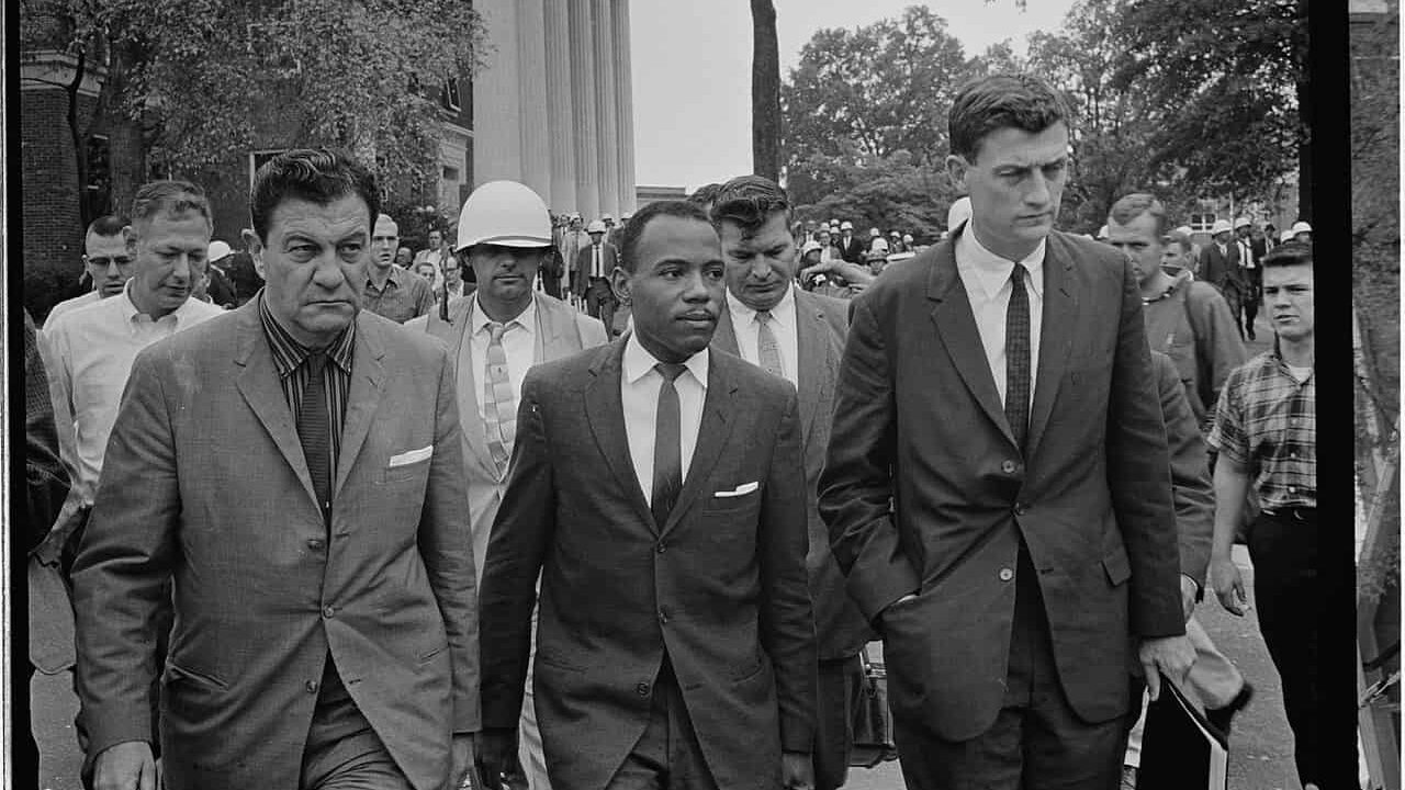 hotograph shows James Meredith walking to class accompanied by U.S. marshals.; James Meredith walking to class at University of Mississippi, accompanied by U.S. marshals. According to http://hdl.loc.gov/loc.pnp/cph.3c35515, the men flanking Meredith are U.S. Marshal James McShane (left) and John Doar of the Justice Department (right)