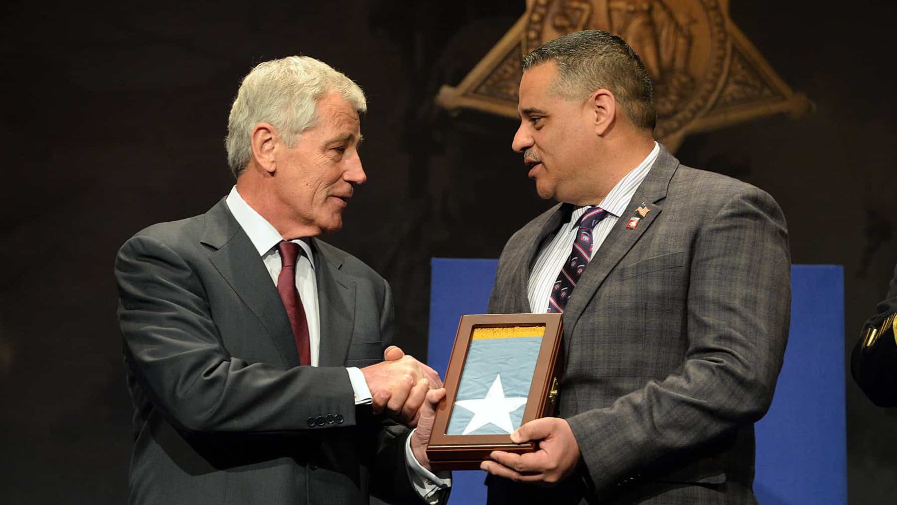 Secretary of Defense Chuck Hagel, left, presents the Medal of Honor Flag to Richard Conde, on behalf of his father Staff Sgt. Felix M. Conde-Falcon, one of 24 Army veterans honored during the Valor 24 Hall of Heroes Induction ceremony, held at the Pentagon, Washington D.C., March 19, 2014.