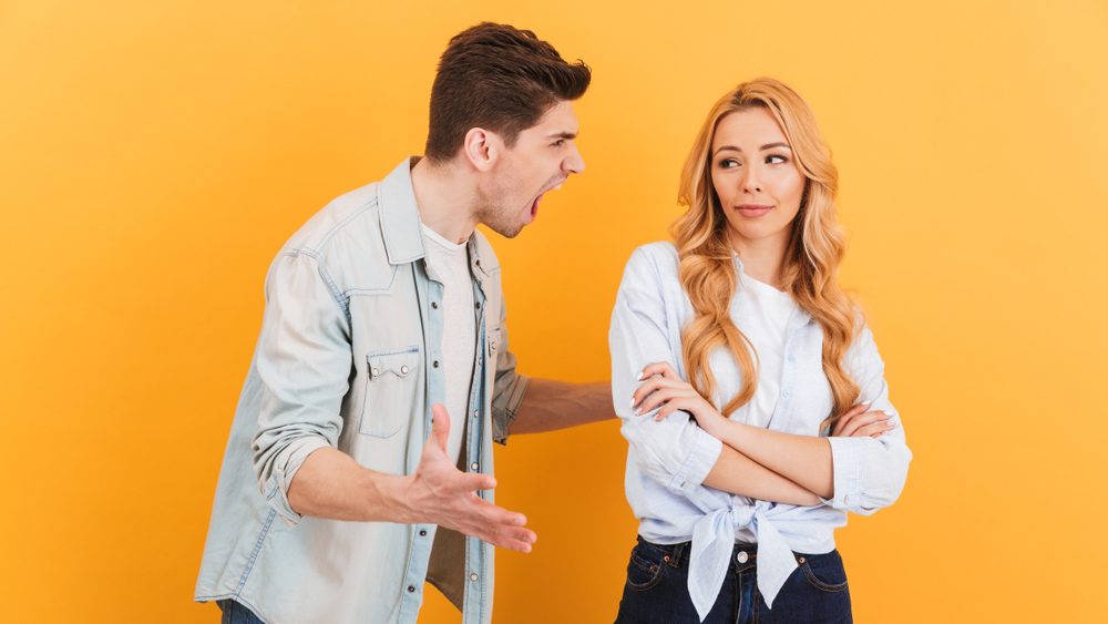 Photo of crazy angry man shouting at calm innocent woman isolated over yellow background