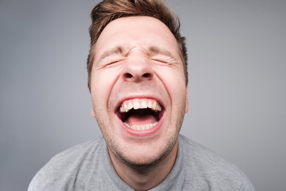 Studio close up shoot of adult man laughing looking at the camera over white background. He is in positive mood and jokes are gold.