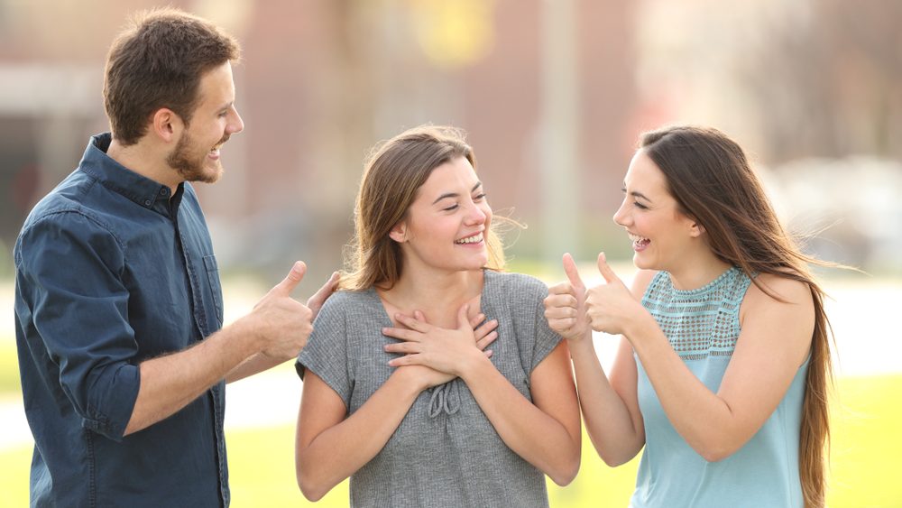 Two friends congratulating a happy girl standing in the street