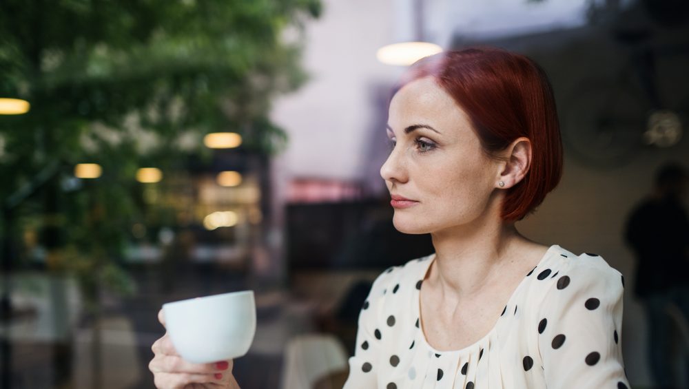 A portrait of woman with coffee sitting at the table in a cafe, shot through glass.