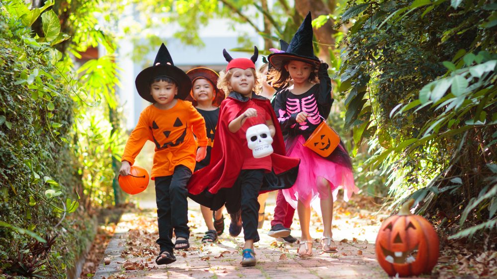 Child in Halloween costume. Mixed race Asian and Caucasian kids trick or treat on suburban street. Little boy and girl with pumpkin lantern and candy bucket. Baby in witch hat. Autumn holiday fun.
