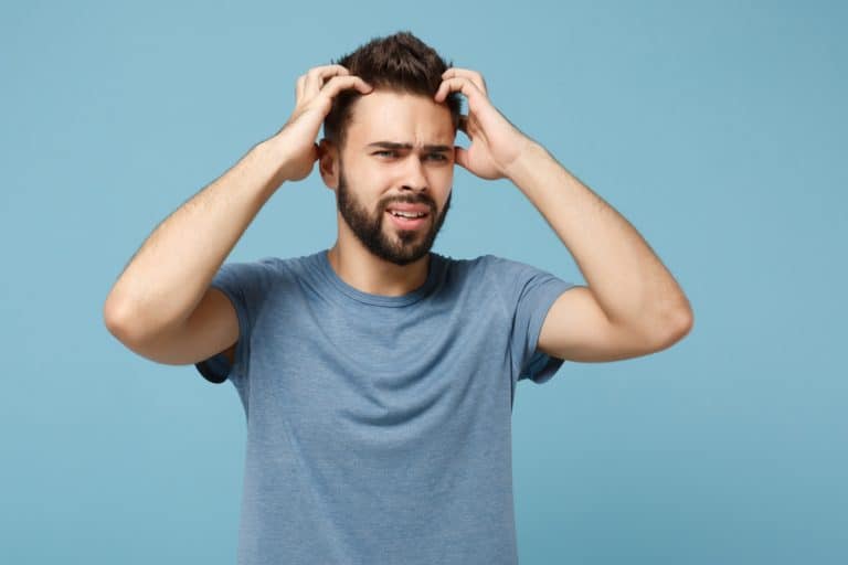 Young nervous preoccupied man in casual clothes posing isolated on blue background studio portrait. People sincere emotions lifestyle concept. Mock up copy space. Looking aside, putting hands on head