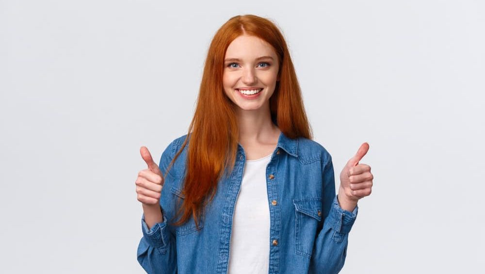 Waist-up portrait alluring confident smiling redhead female blogger review awesome new product, showing thumbs-up in approval, like or agree gesture, standing white background