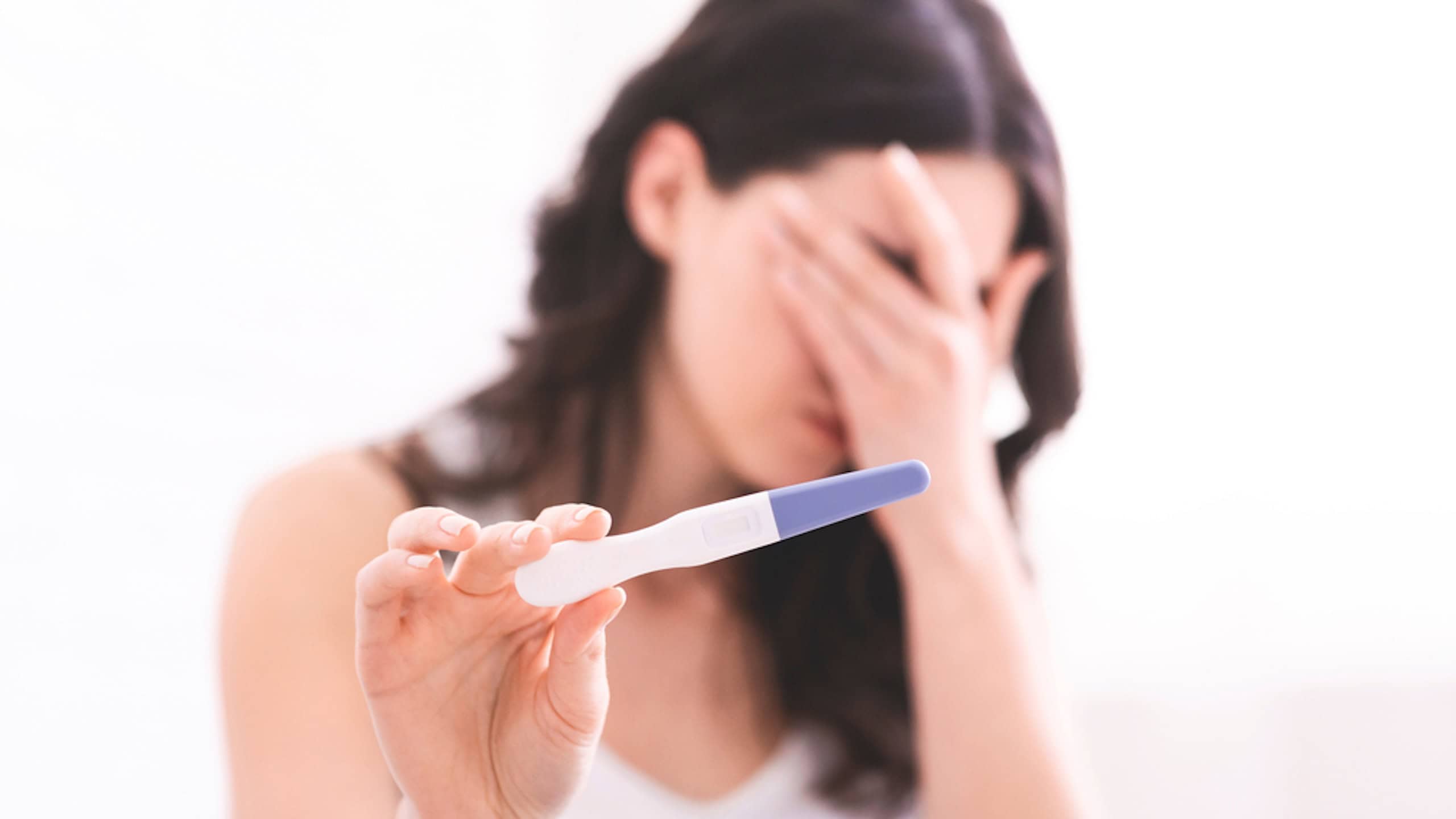 Unexpected result. Desperate young woman showing result of pregnancy test on camera, hiding her face