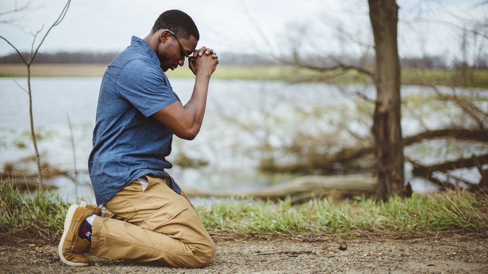 A vertical shot of an African-American male praying on his knees