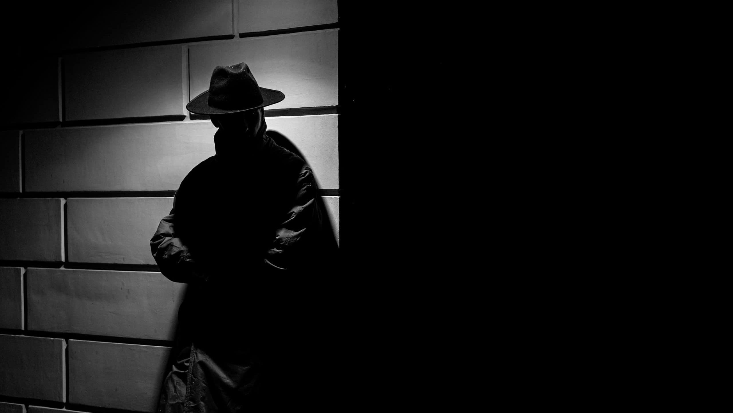 dark silhouette of a man in a raincoat with a hat at night on the street in a crime Noir style
