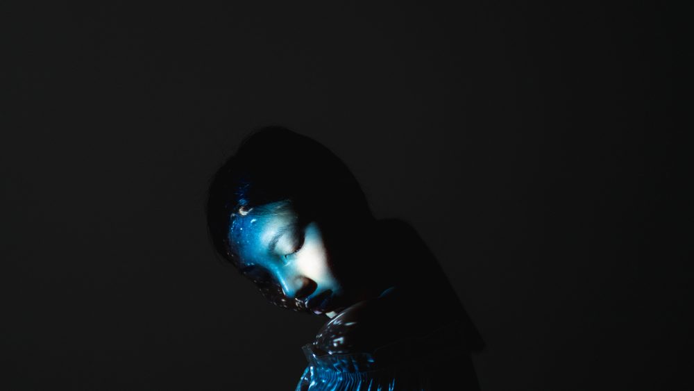 Art portrait. Soul harmony. Reincarnation destiny. Karma afterlife. Blue color peaceful Asian woman face silhouette with closed eyes abstract pattern light isolated on black copy space background.