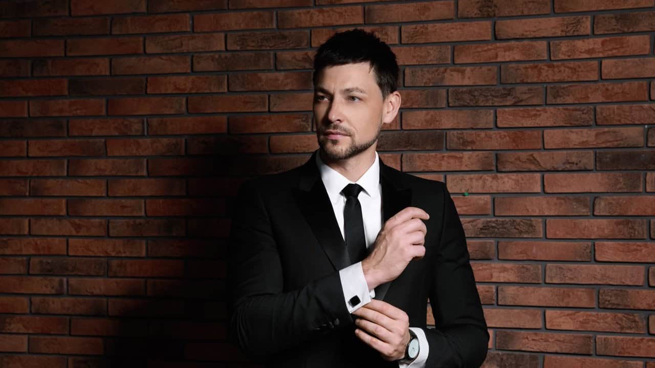 Man wearing stylish suit and cufflinks near brick wall
