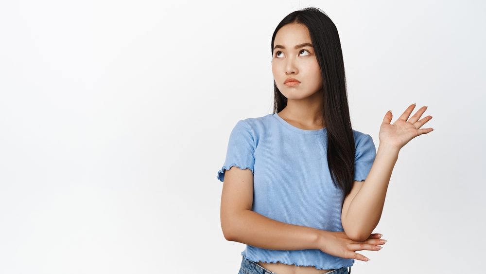 Annoyed arrogant asian woman roll eyes, looking away and wave hand to decline smth bothering her, standing over white background