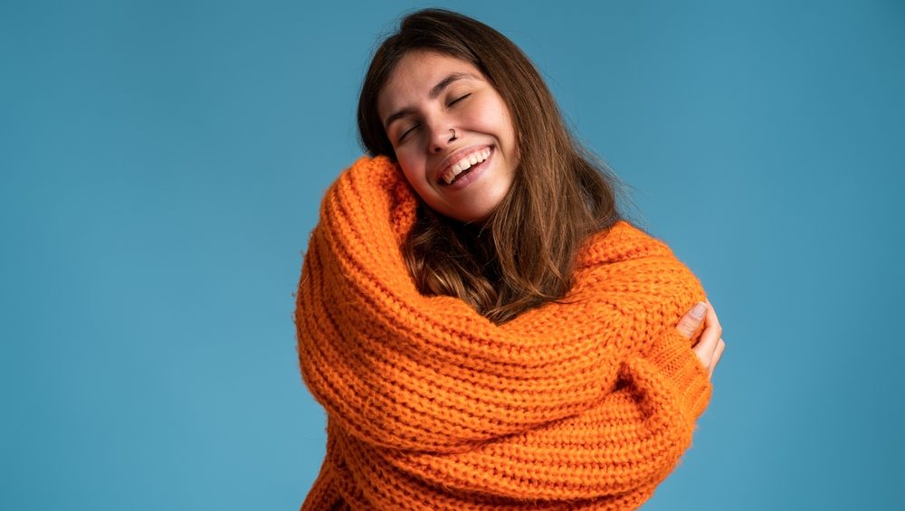 I love myself. Portrait of pleased satisfied girl hugging herself and smiling, feeling comfortable and fulfilled, narcissistic egoistic person. Indoor studio shot blue background