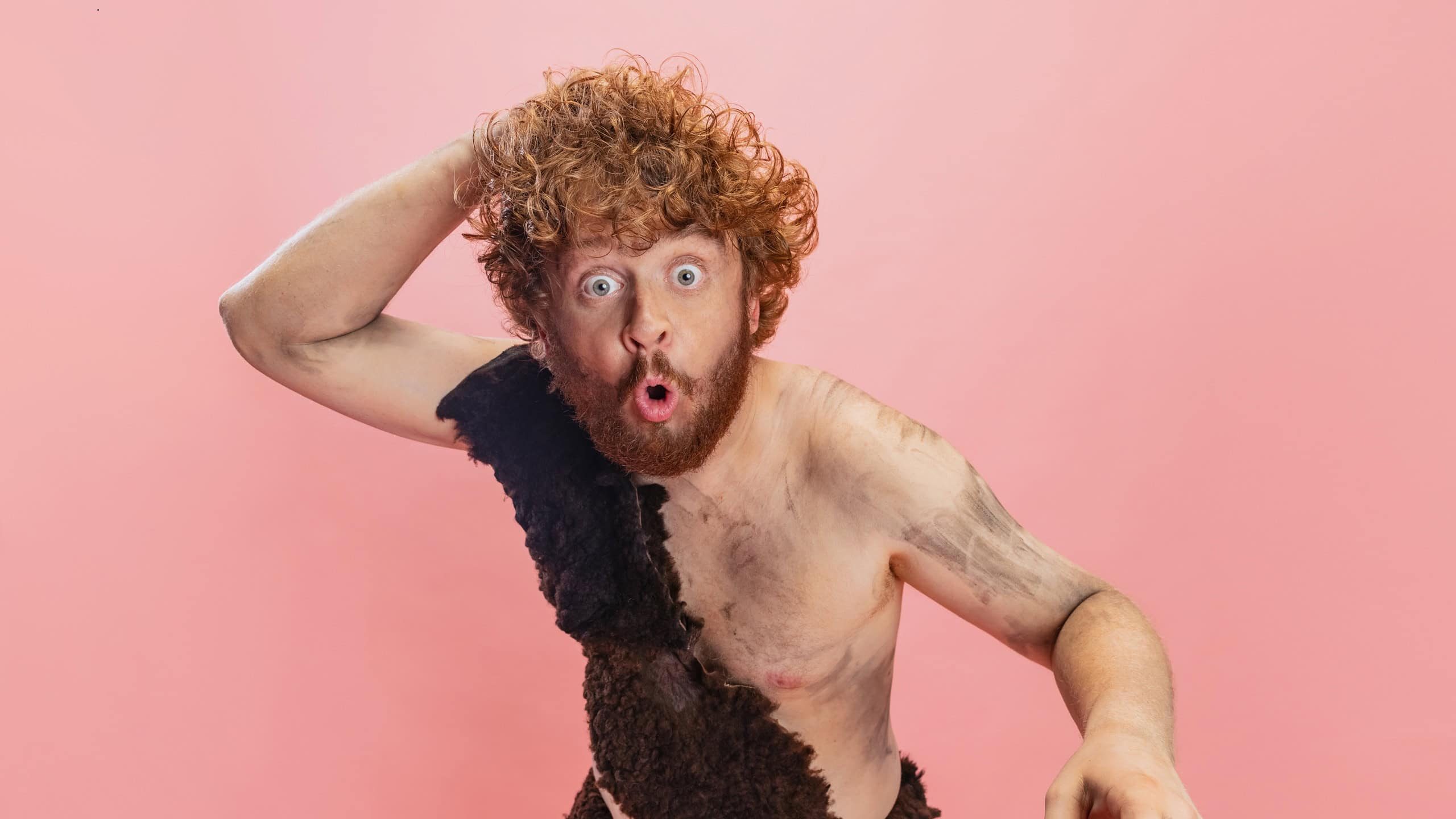Portrait of man in character of neandertal scratching back of his head isolated over pink background. Shocked facial expression. Concept of history, modern and ancient combination, evolution and ad