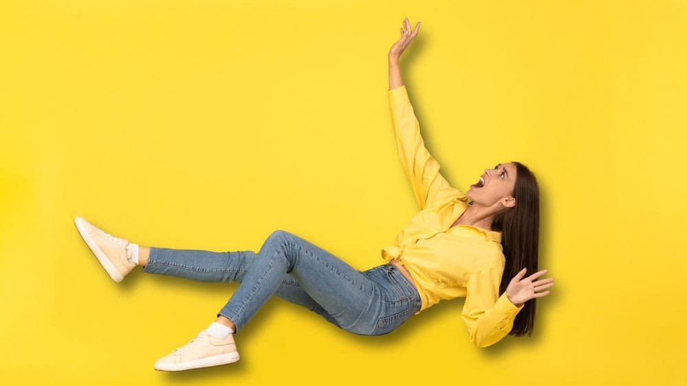Scared Millennial Lady Falling In Mid Air And Shouting Posing Over Yellow Studio Background. Emotional Woman Experiencing Zero Gravity And Screaming In Fear. Acrophobia And Weightlessness Concept