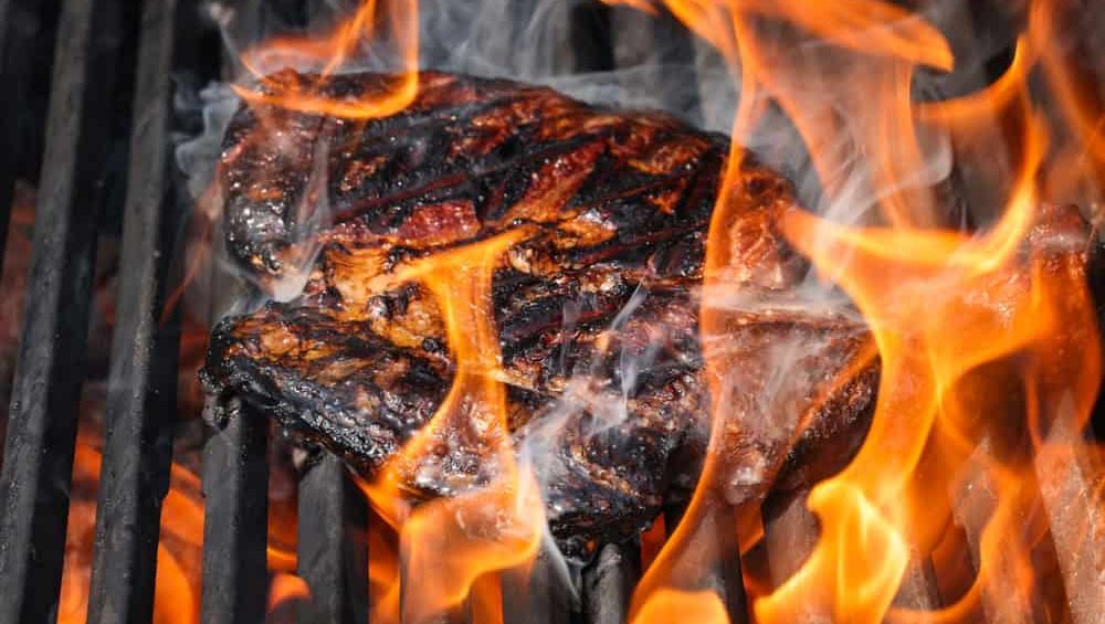 Close up searing and smoking ribeye beef steaks on open fire outdoor grill with cast iron metal grate, high angle view