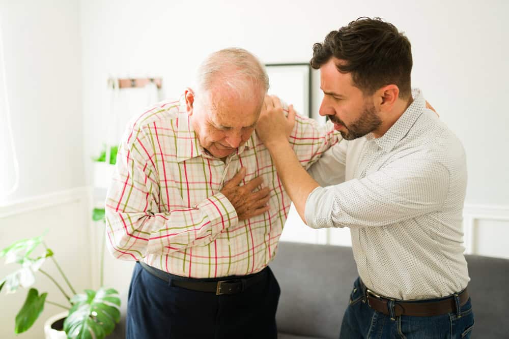 Ill old caucasian man suffering a heart attack and needing medical emergency services getting help from his stressed young son