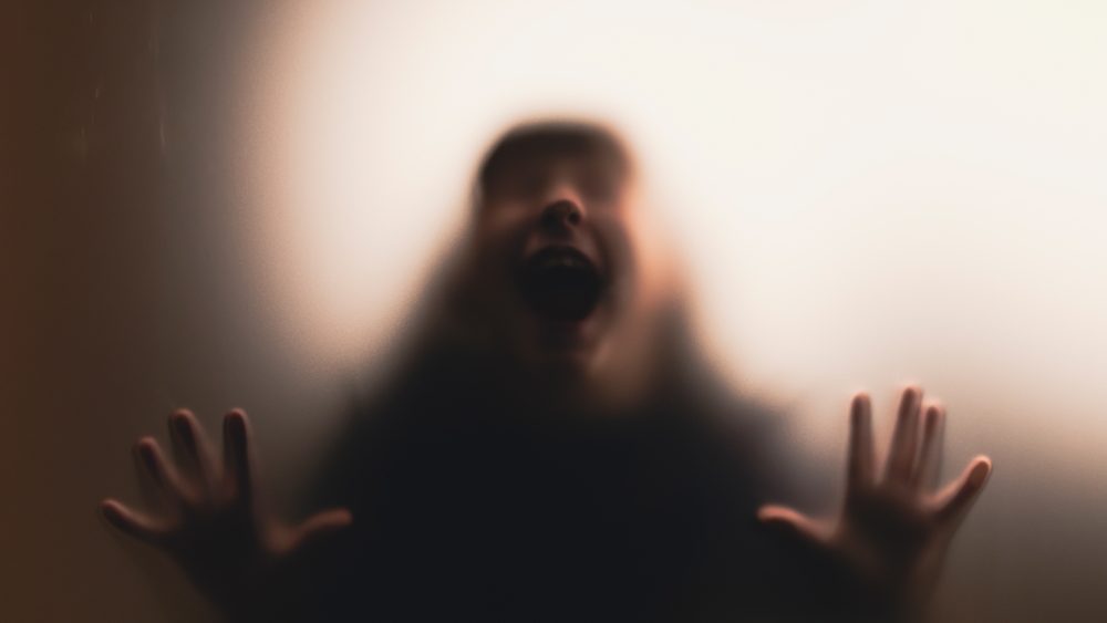Scared, screaming girl behind the matte glass. Halloween festival concept.