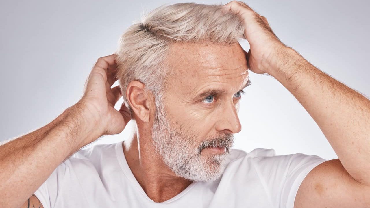 Mature man with silver hair touching his head, looking thoughtful and confident.