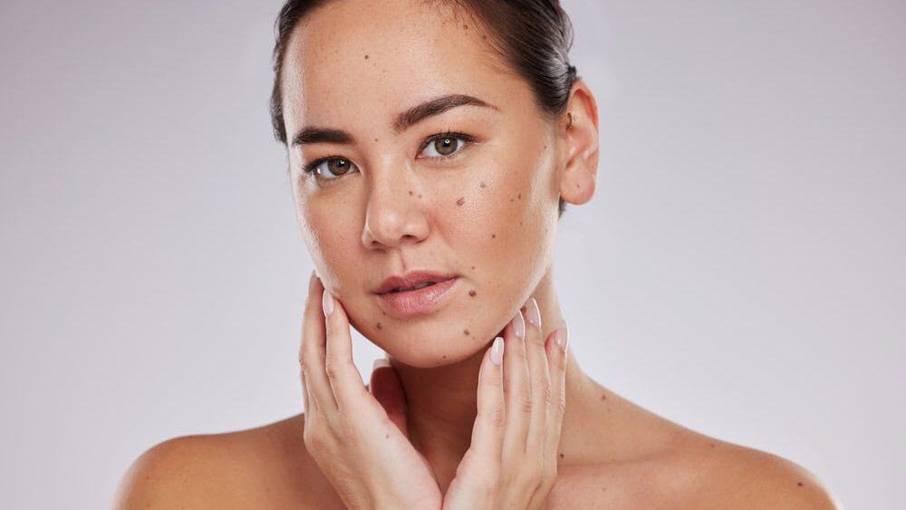 Asian woman, face beauty and skincare portrait in studio for dermatology cosmetic and skin glow. Aesthetic model person with hand for makeup shine and luxury facial self care on grey background
