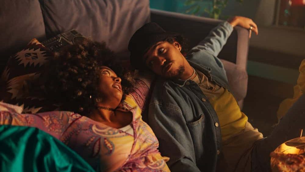 A young diverse couple is at home, chilling sitting on the floor and leaning on a sofa.
