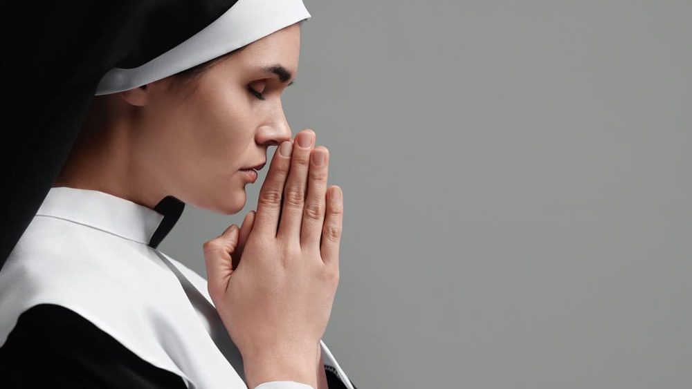 Nun with clasped hands praying to God on grey background. Space for text