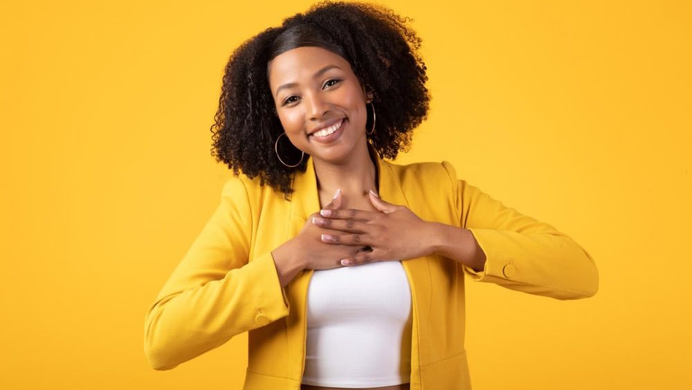 Thank you. Thankful black lady pressing hands to chest and smiling, standing posing over yellow studio background. Gratitude and kindness concept